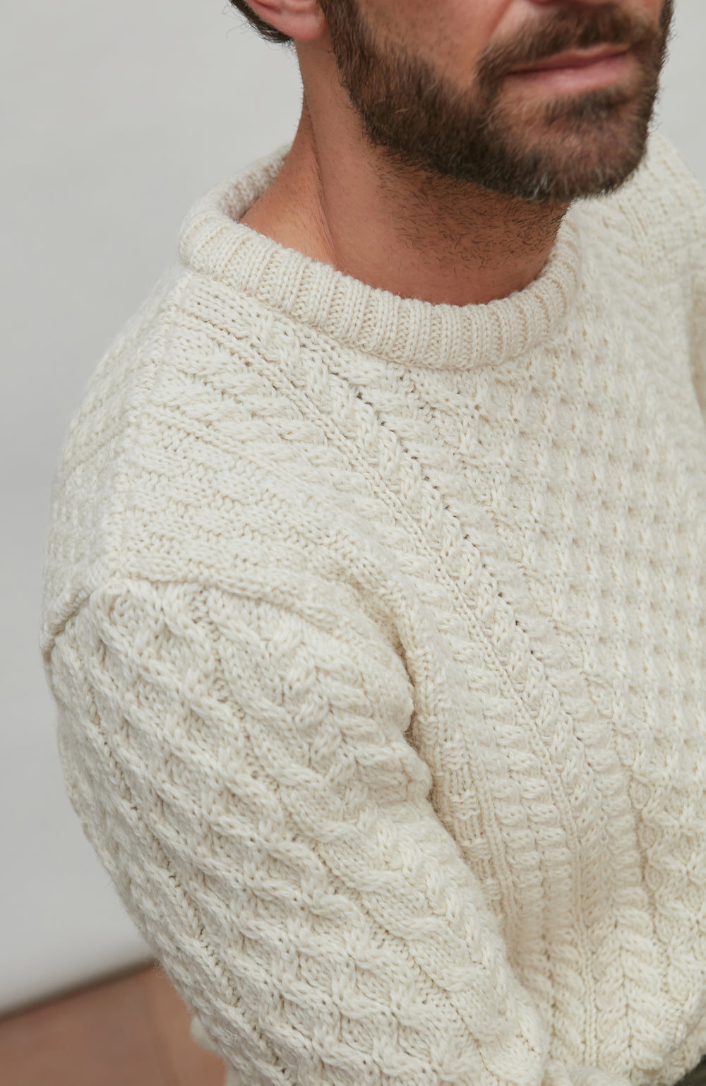 Close-up of a person wearing a cream-colored cable knit sweater against a neutral background