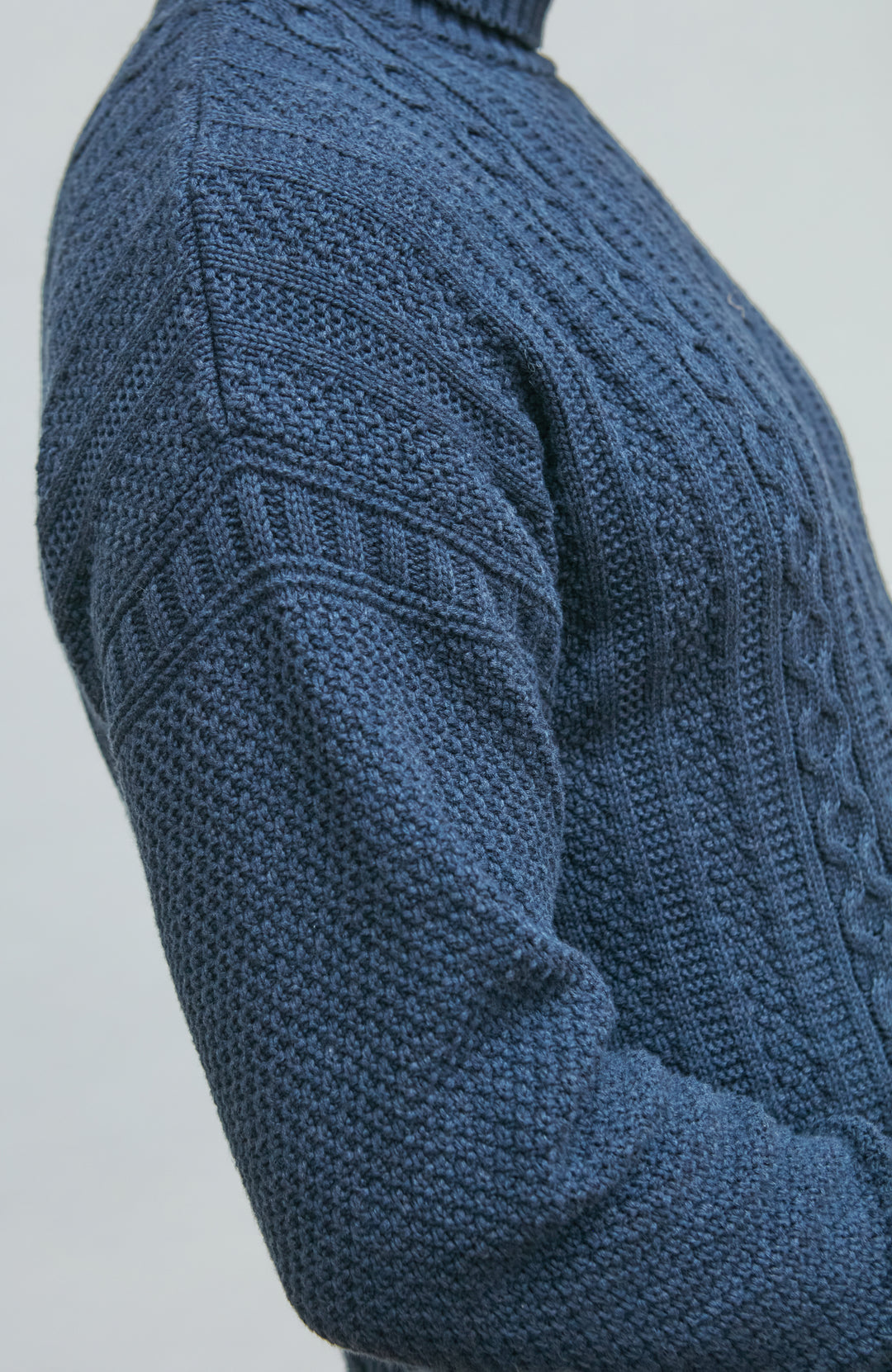 Close-up of a blue knitted sweater with intricate patterns on a light gray background