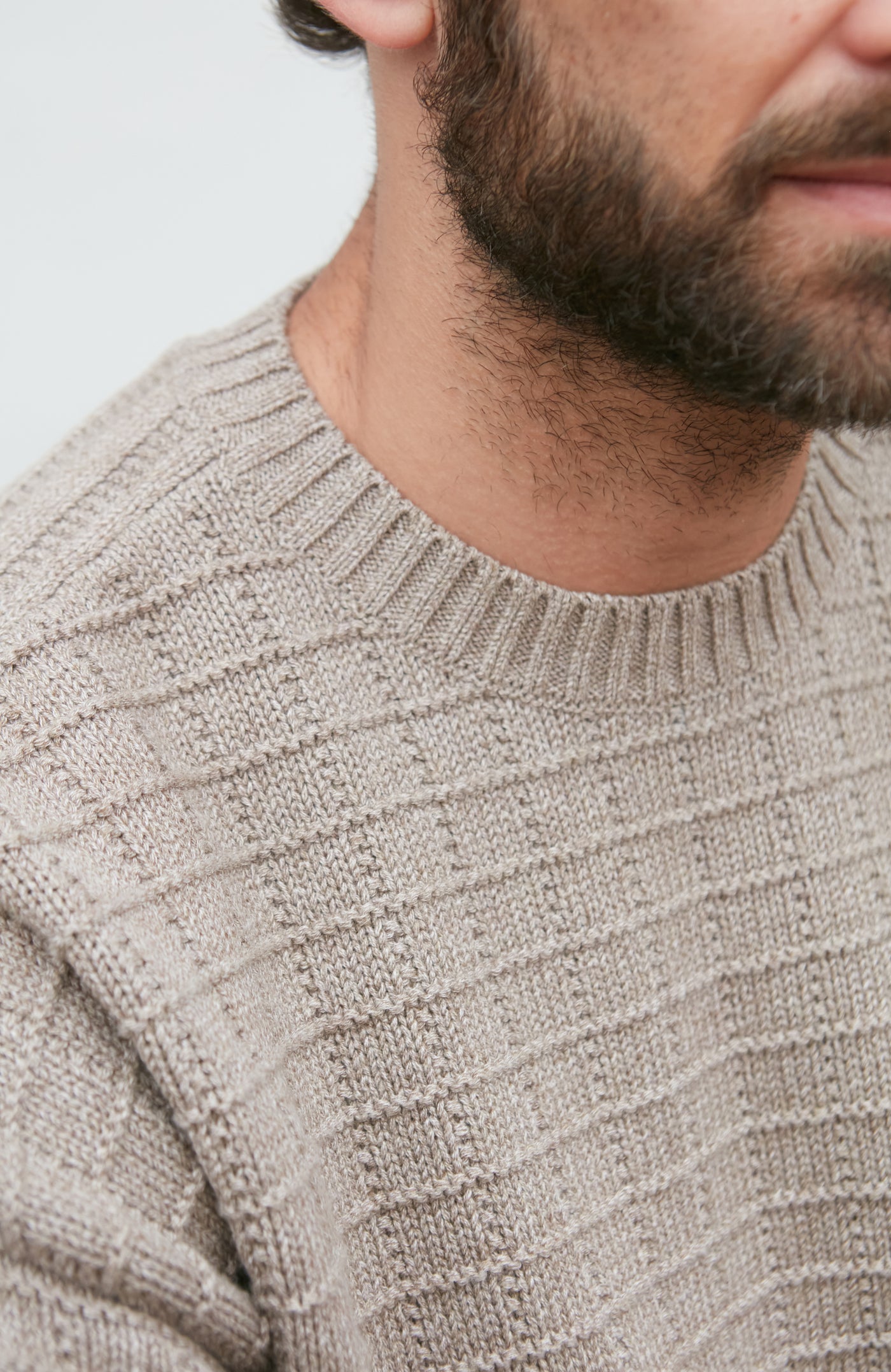 Close-up of a person wearing a textured beige sweater with a blurred background