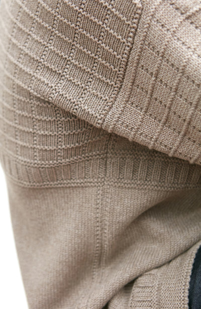 Close-up of a beige knitted gurnsey sweater with a textured pattern.