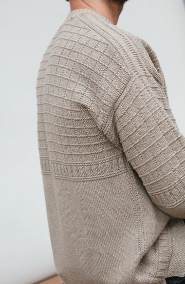 Close-up of a beige fishermans knitted sweater on a plain background