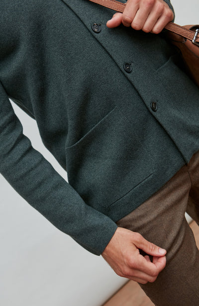 Person wearing a dark green mandarin collar jacket jacket with a brown bag on a light gray background