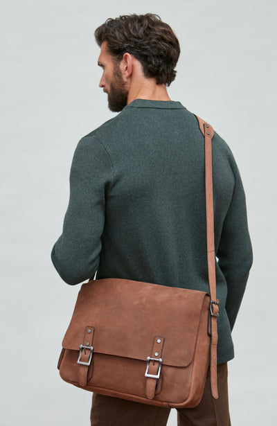 Man wearing a dark green mandarin collar jacket and brown leather satchel bag on a plain background