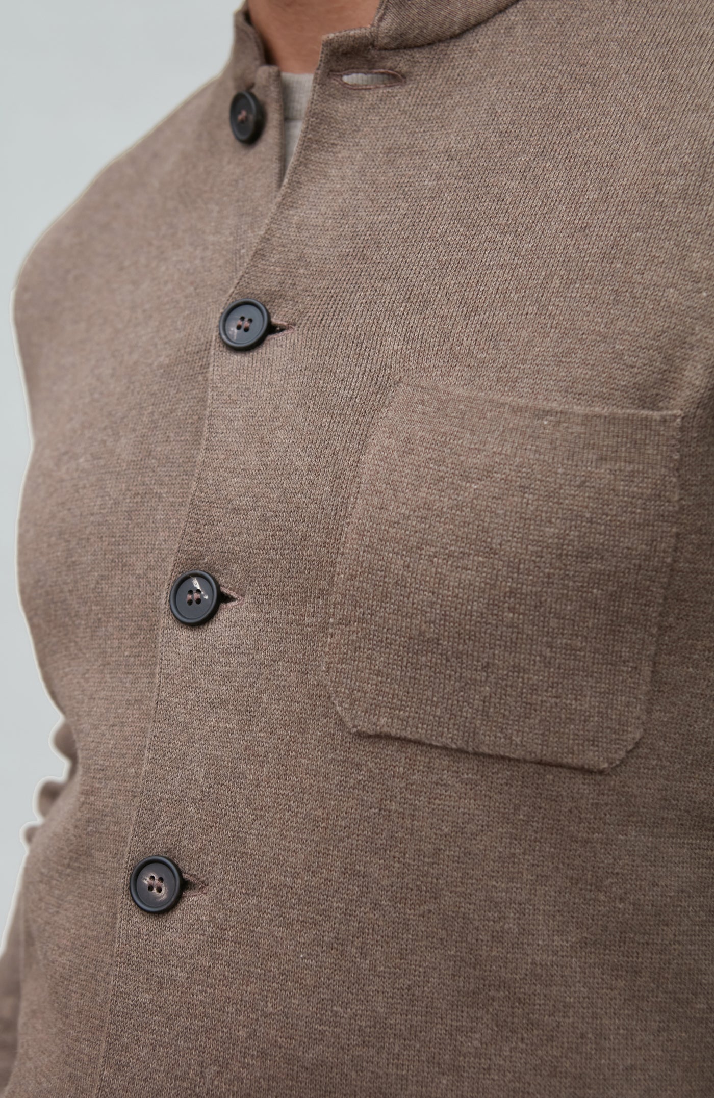 Close-up of a brown mandarin collar jacket  garment with buttons and a pocket on a light gray background