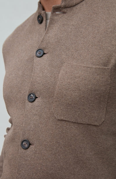 Close-up of a brown mandarin collar jacket  garment with buttons and a pocket on a light gray background