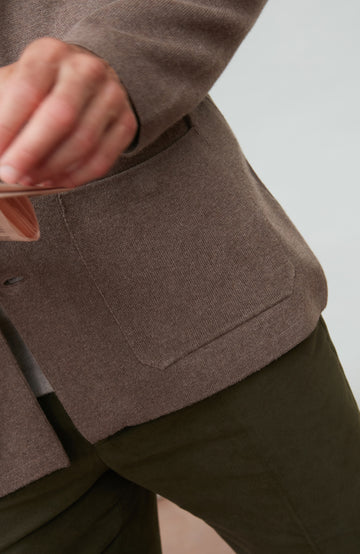 Close-up of a person wearing a brown mandarin collar jacket with a neutral background