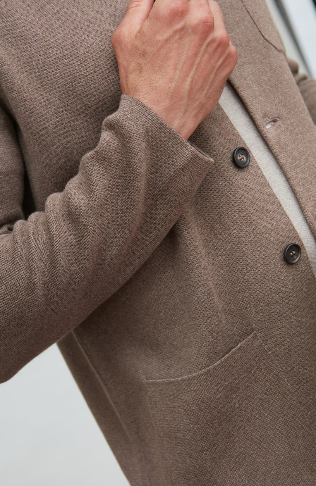 Close-up of a brown mandarin collar jacket  with a hand adjusting the sleeve on a light gray background