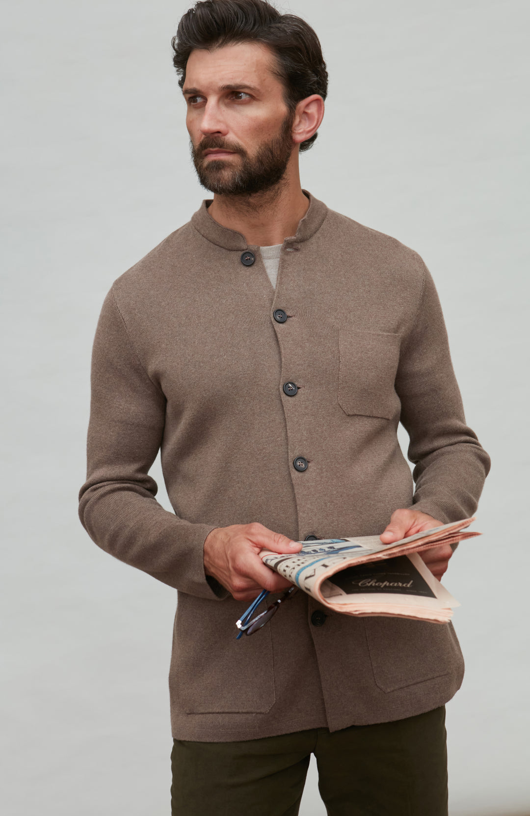 Man wearing a brown mandarin collar jacket holding a book against a plain background