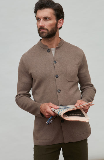Man wearing a brown mandarin collar jacket holding a book against a plain background