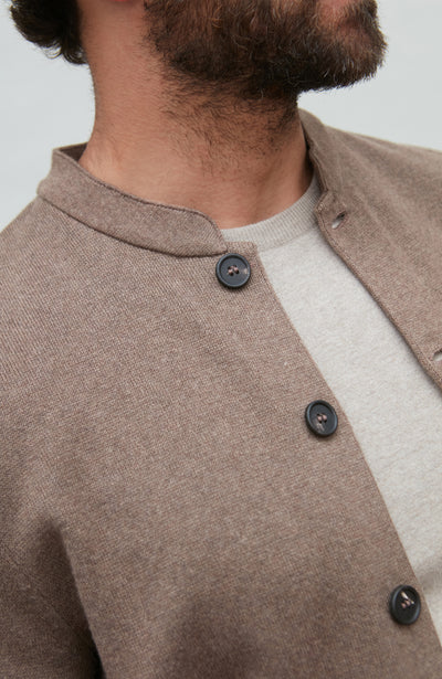 Close-up of a person wearing a brown mandarin collar jacket with buttons on a neutral background