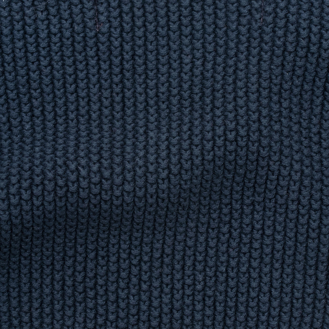 Woman wearing a blue knitted neck tie and scarf against a plain background by Paul James