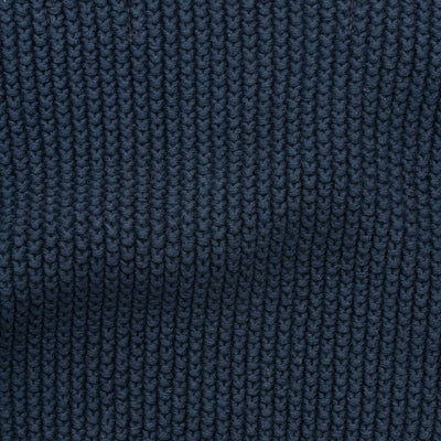 Woman wearing a blue knitted neck tie and scarf against a plain background