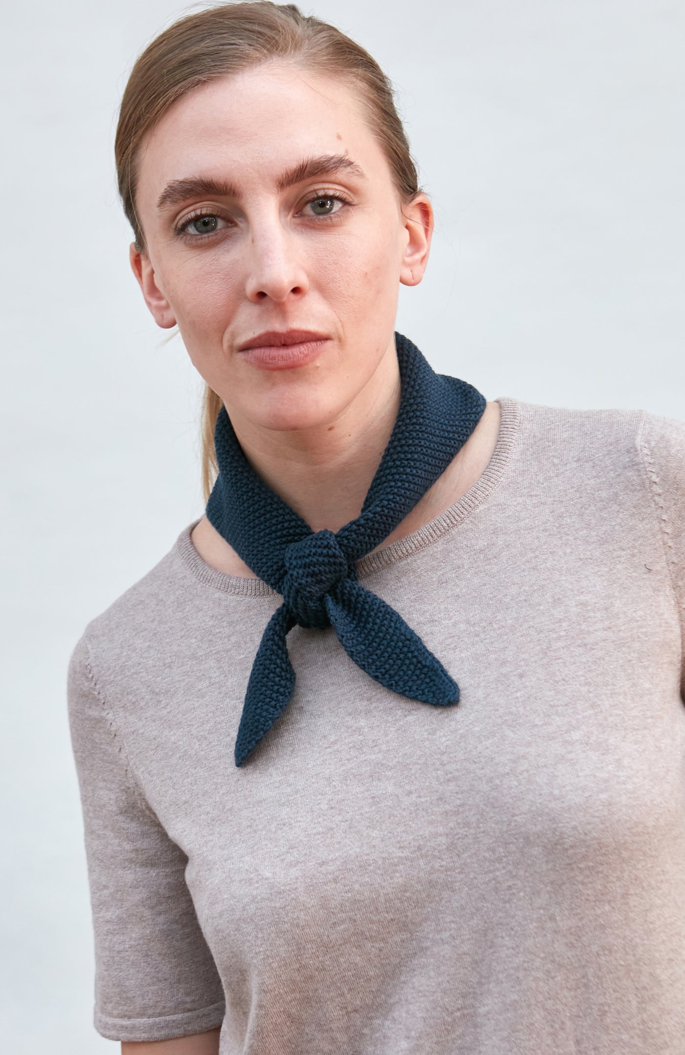 Woman wearing a blue knitted neck tie and scarf against a plain background