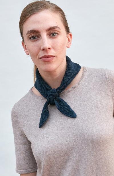Woman wearing a blue knitted neck tie and scarf against a plain background