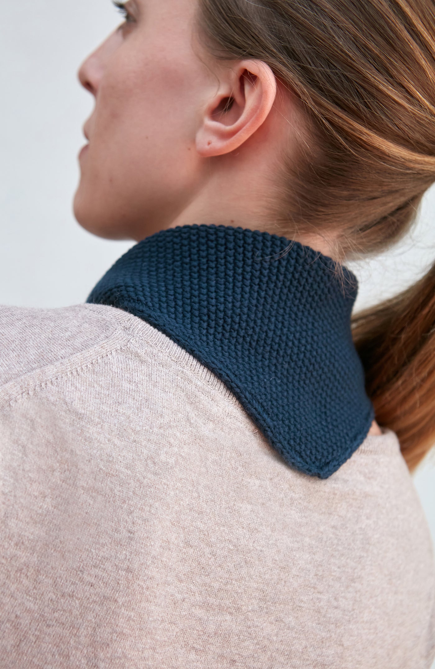 Woman wearing a blue knitted neck tie and scarf against a plain background