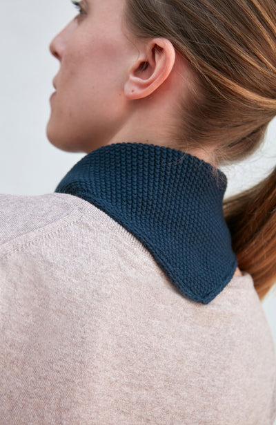 Woman wearing a blue knitted neck tie and scarf against a plain background