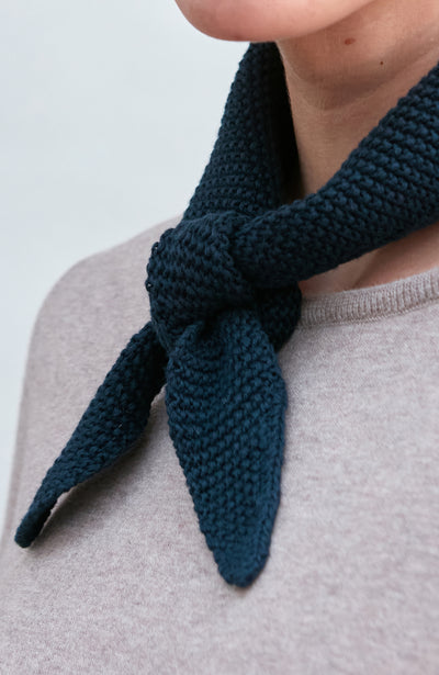 Woman wearing a blue knitted neck tie and scarf against a plain background