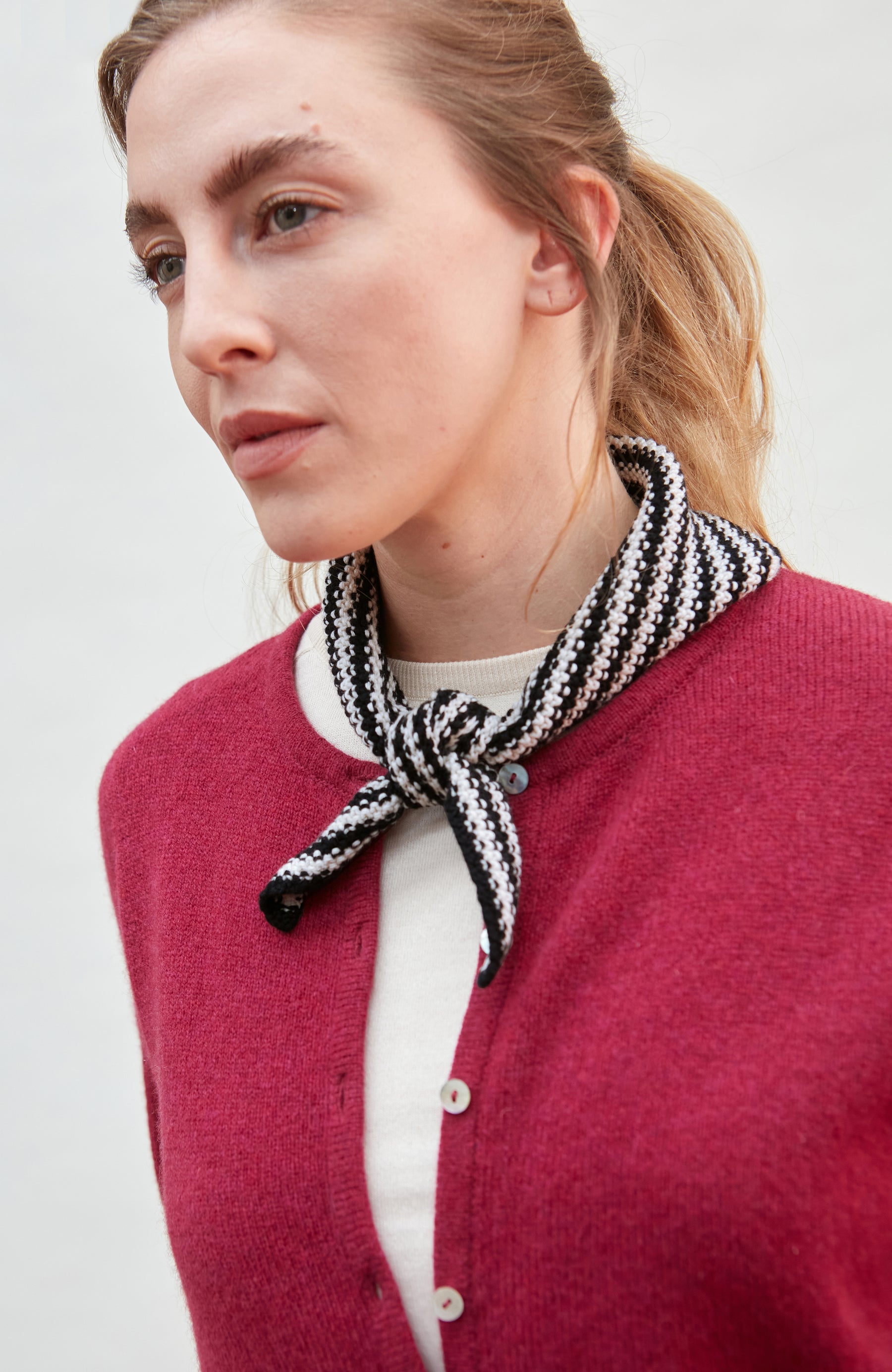 Woman wearing a black and white patterned scarf with a red cardigan on a plain background