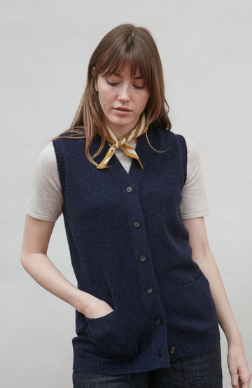 Woman wearing a navy wool blue vest over a white shirt with a yellow stripe bandana scarf, against a plain background by Paul James