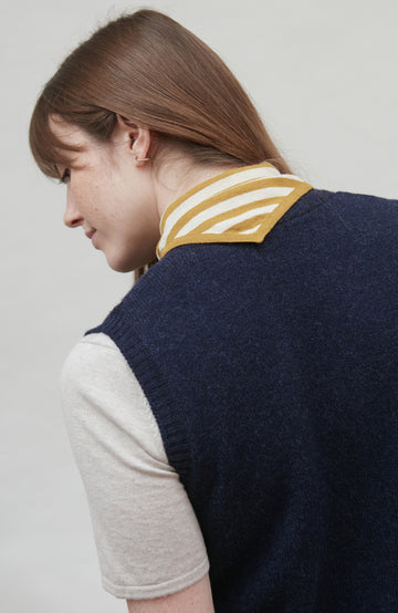 Person wearing a navy wool blue knitted vest over a light gray shirt with a white background by Paul James