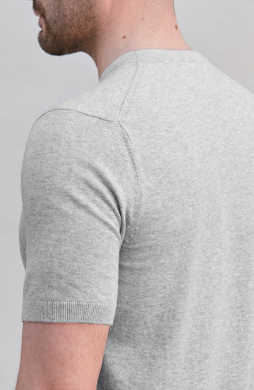 Close-up back view of a man wearing a light heather gray short-sleeve knit shirt against a plain light gray background.