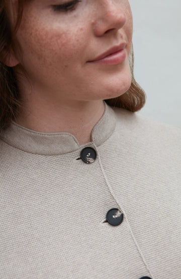 Close-up of a woman wearing a light-colored nehru jacket with black buttons.