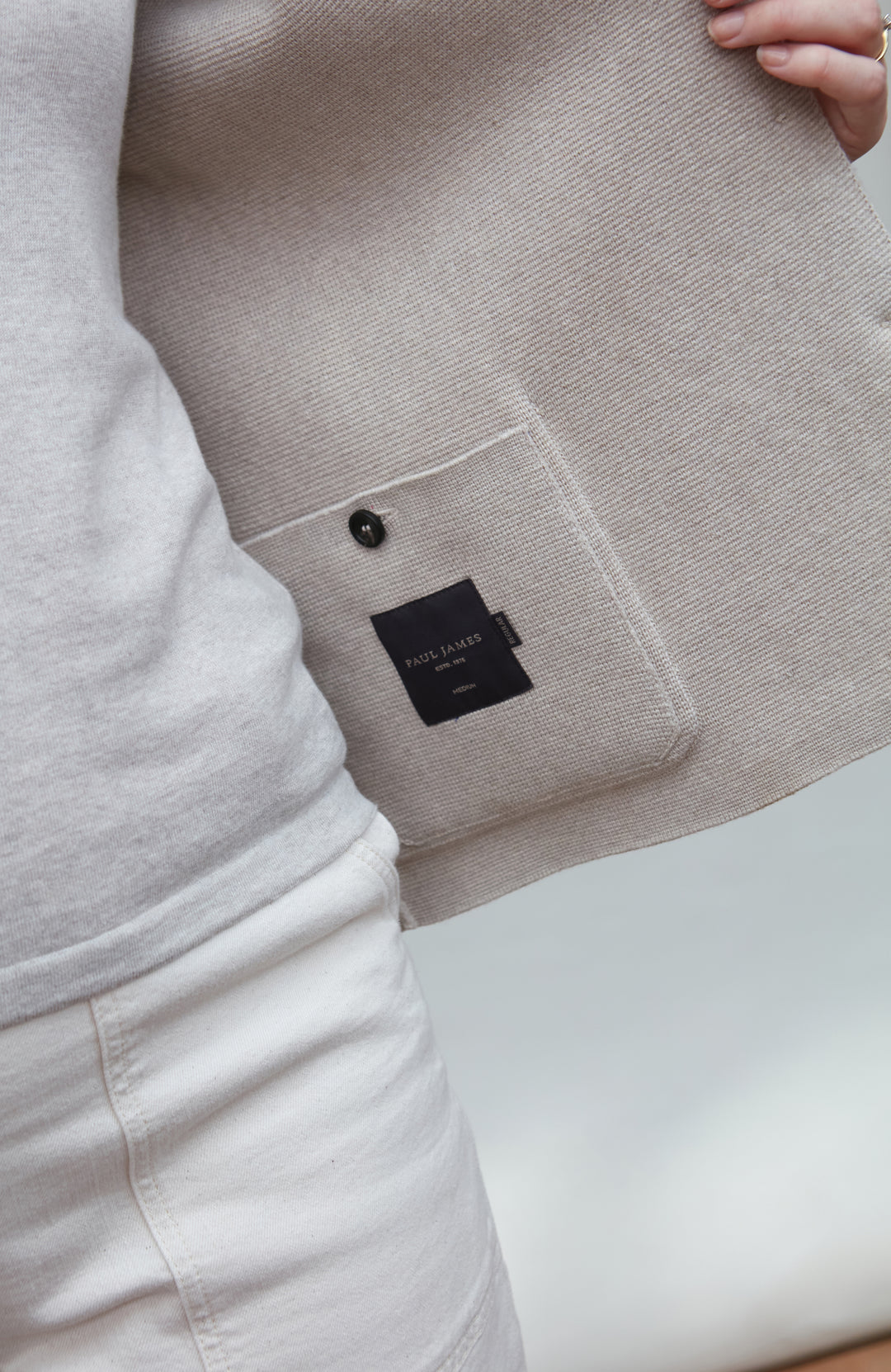 Close-up of a beige jacket with a black label on inside pocket on a white background