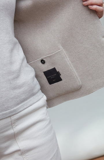 Close-up of a beige jacket with a black label on inside pocket on a white background