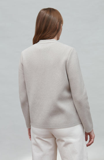 Person wearing a light gray nehru jacket and white pants on a plain background