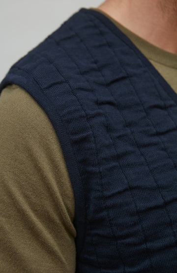 Navy quilted vest worn over a green shirt against a neutral background