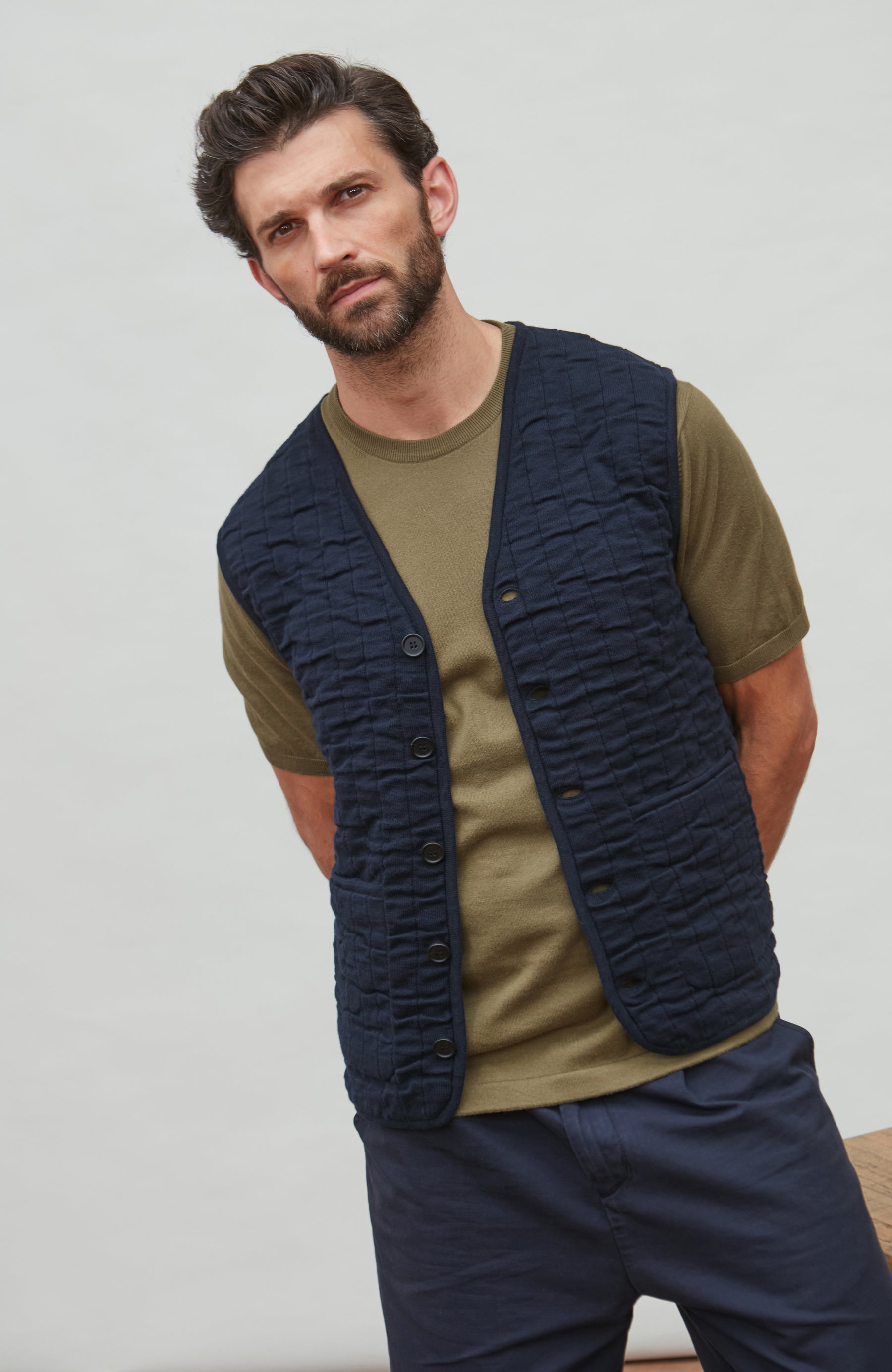 Man wearing a navy quilted vest over a green shirt with a neutral background
