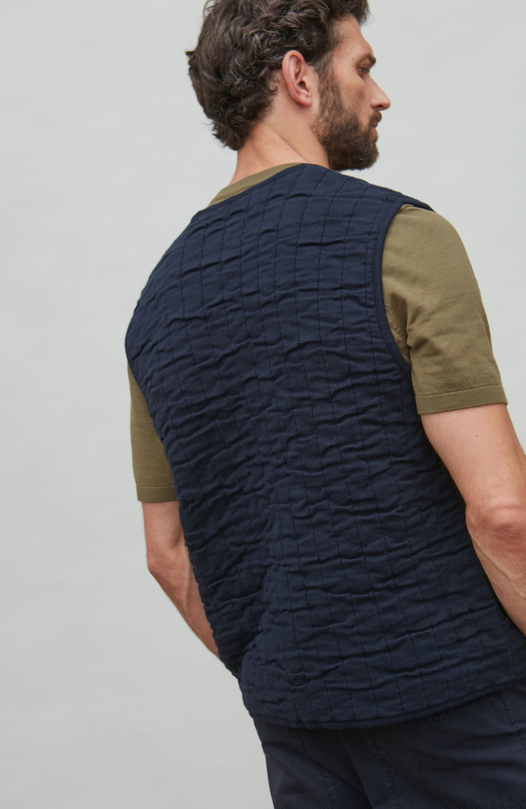 Man wearing a navy quilted vest over a green shirt on a plain background