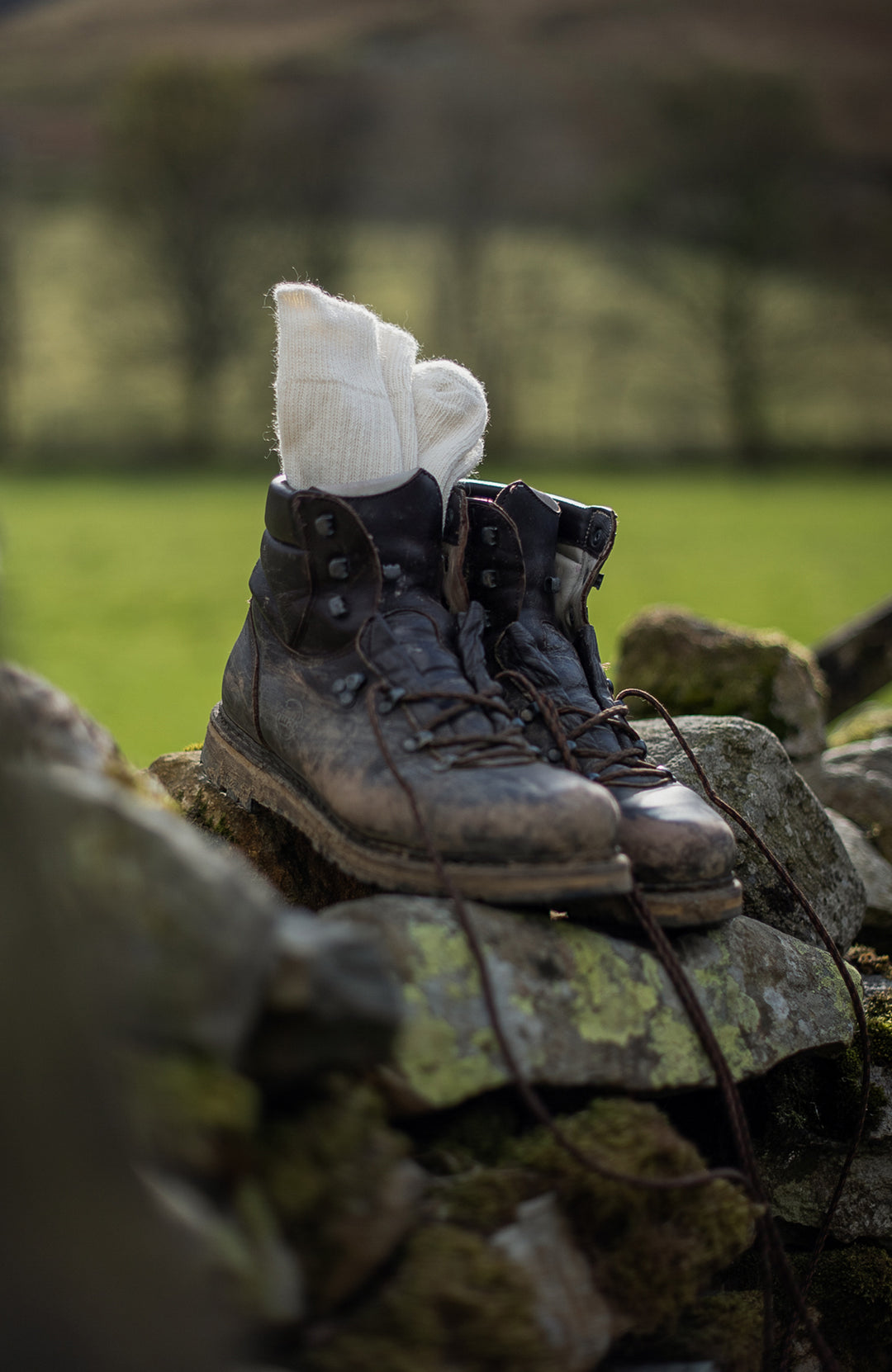 Pair of worn boots with a white sock on a stone wall outdoors