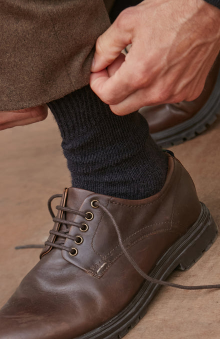 Person wearing a brown alpaca socks and shoe and dark sock on a neutral background by Paul James 