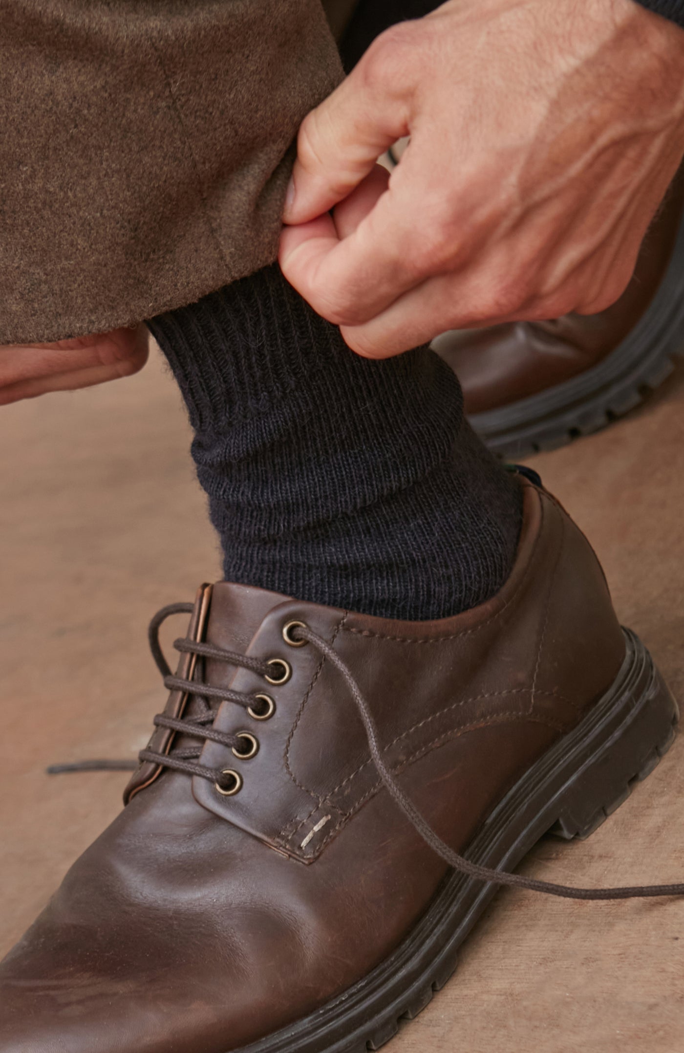 Person wearing a brown alpaca socks and shoe and dark sock on a neutral background