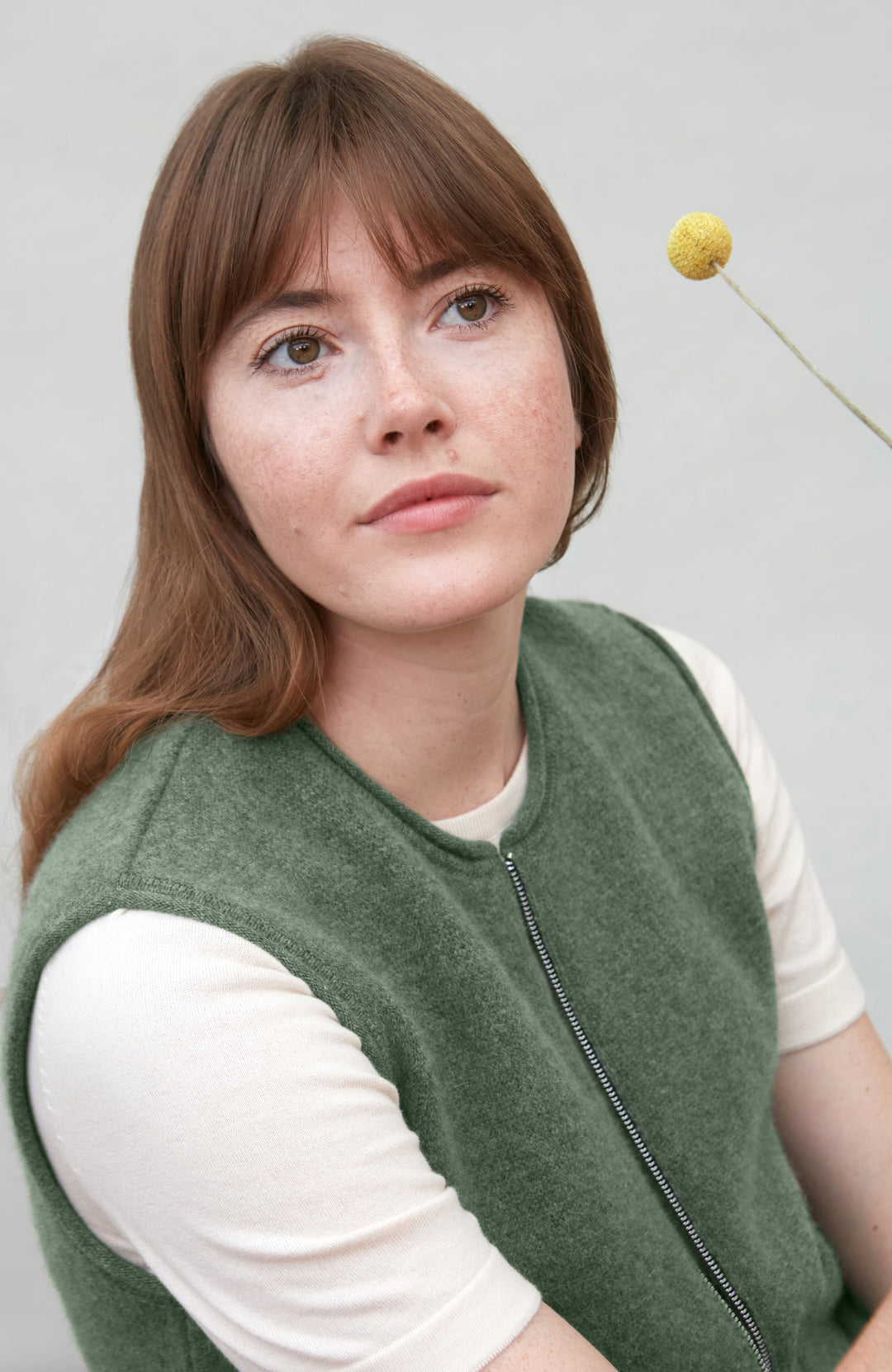 Woman wearing a green wool gilet by paul james over a white shirt with a neutral background