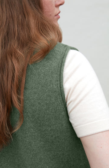 woman wearing a green wool gilet by paul james over a white shirt with a neutral background