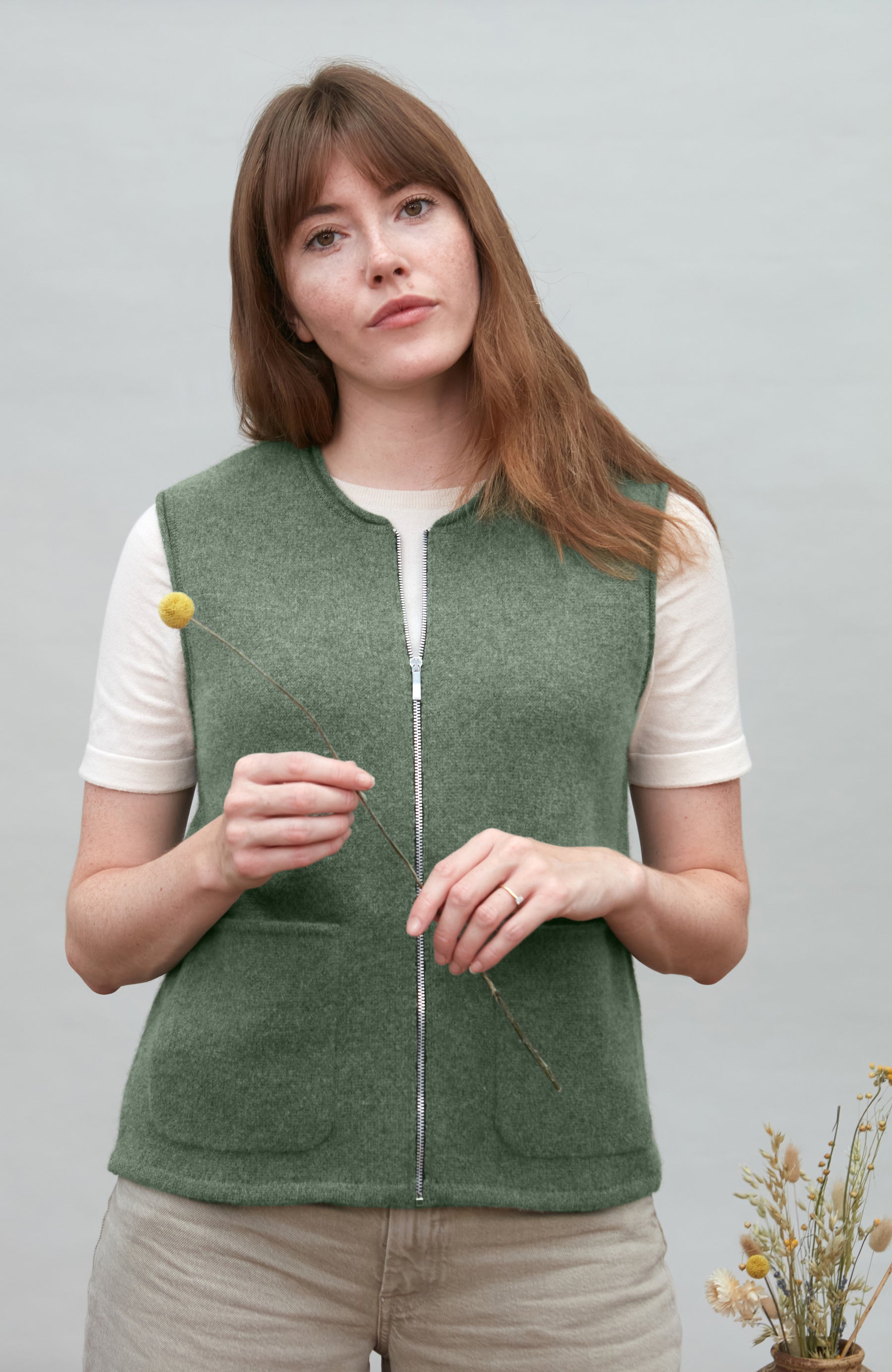 Woman wearing a green wool gilet by paul james over a white shirt on a light gray background