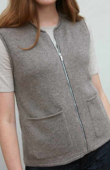 Person wearing a gray zip-up wool gilet by paul james over a light shirt against a plain background