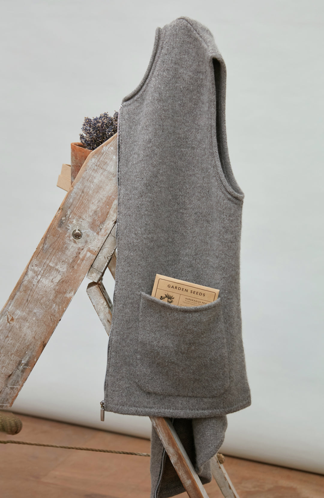 Gray sleeveless wool gilet by paul james with a brand label on a wooden ladder against a white wall.