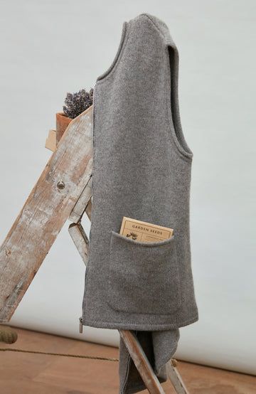 Gray sleeveless wool gilet by paul james with a brand label on a wooden ladder against a white wall.