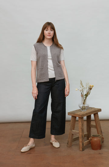 Woman wearing a gray wool gilet by paul james over a white shirt with black pants, standing in a minimalistic room.