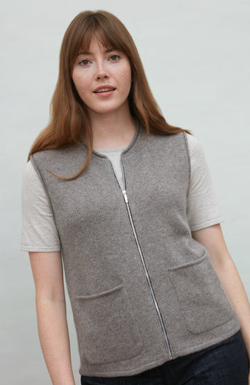 Woman wearing a gray zip-up wool gilet by paul james over a white shirt on a plain background