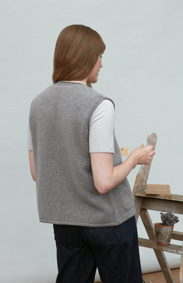 Person wearing a gray wool gilet by paul james holding a paintbrush in a workshop setting