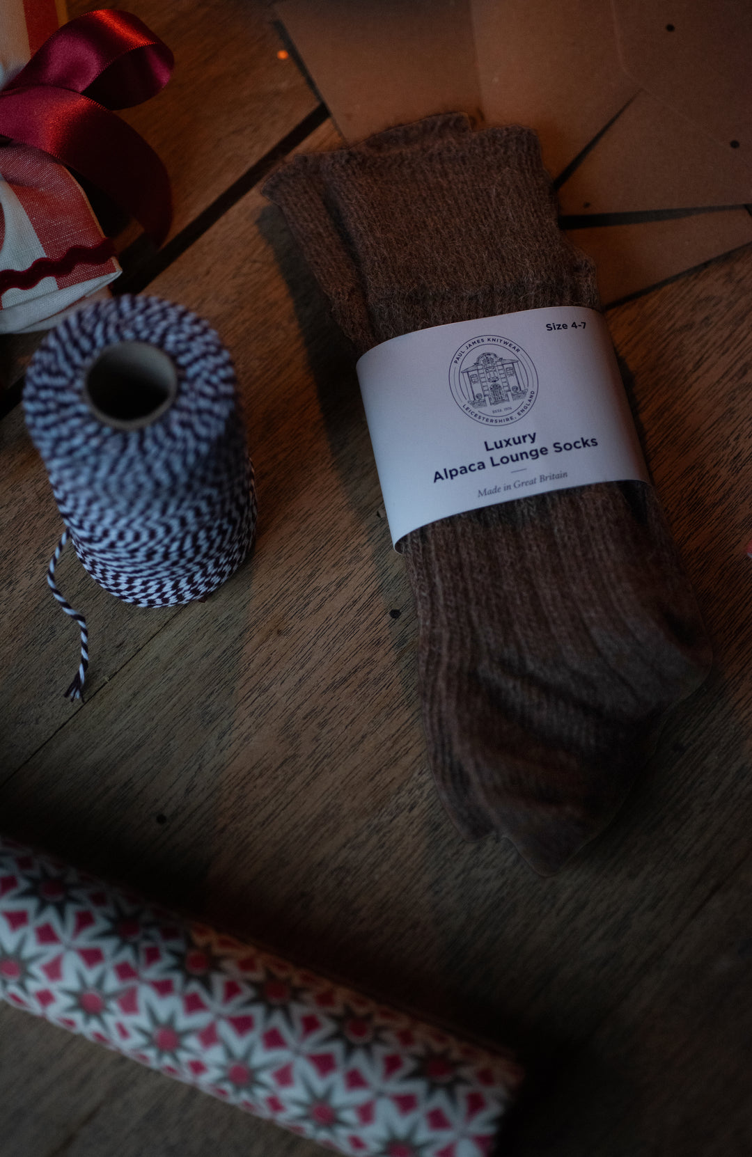 Brown alpaca lounge socks with a label on a wooden surface made in England by Paul James Knitwear.