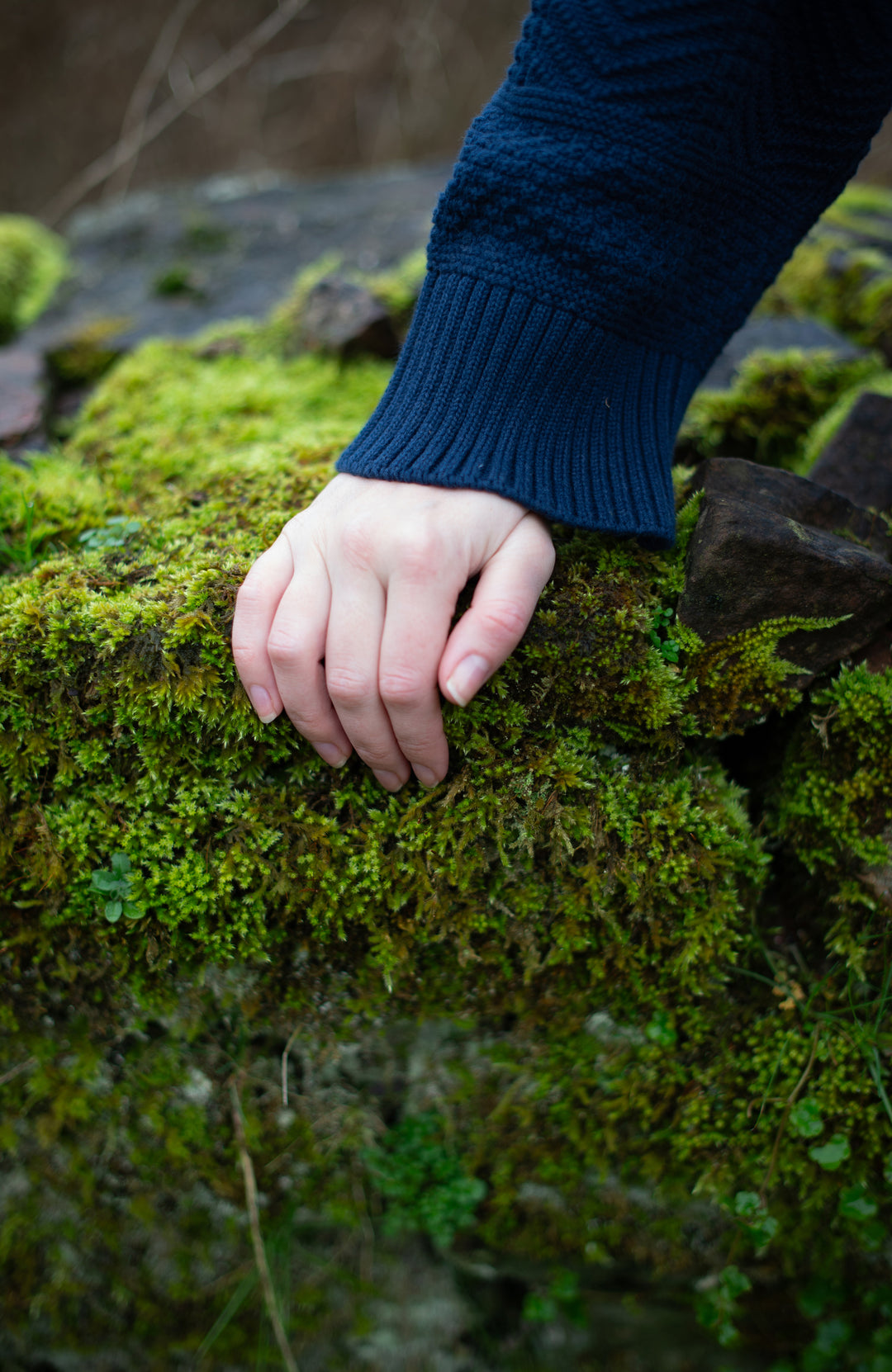 Hand on a moss-covered rock with a blue sweater sleeve by paul james knitwear