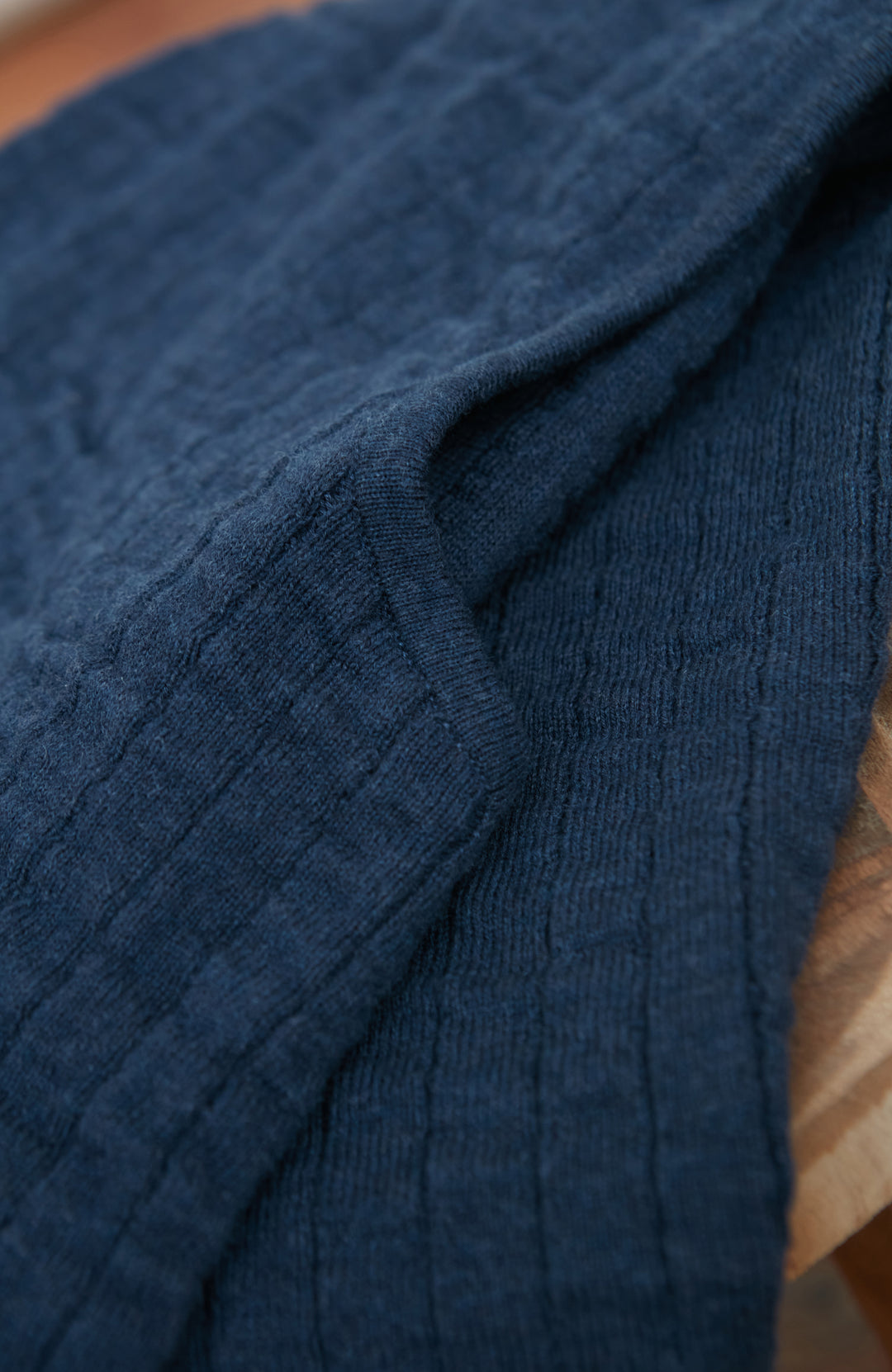 A close-up of a dark navy blue ribbed knit fabric, showing the detailed texture and folds of the material by Paul James Knitwear