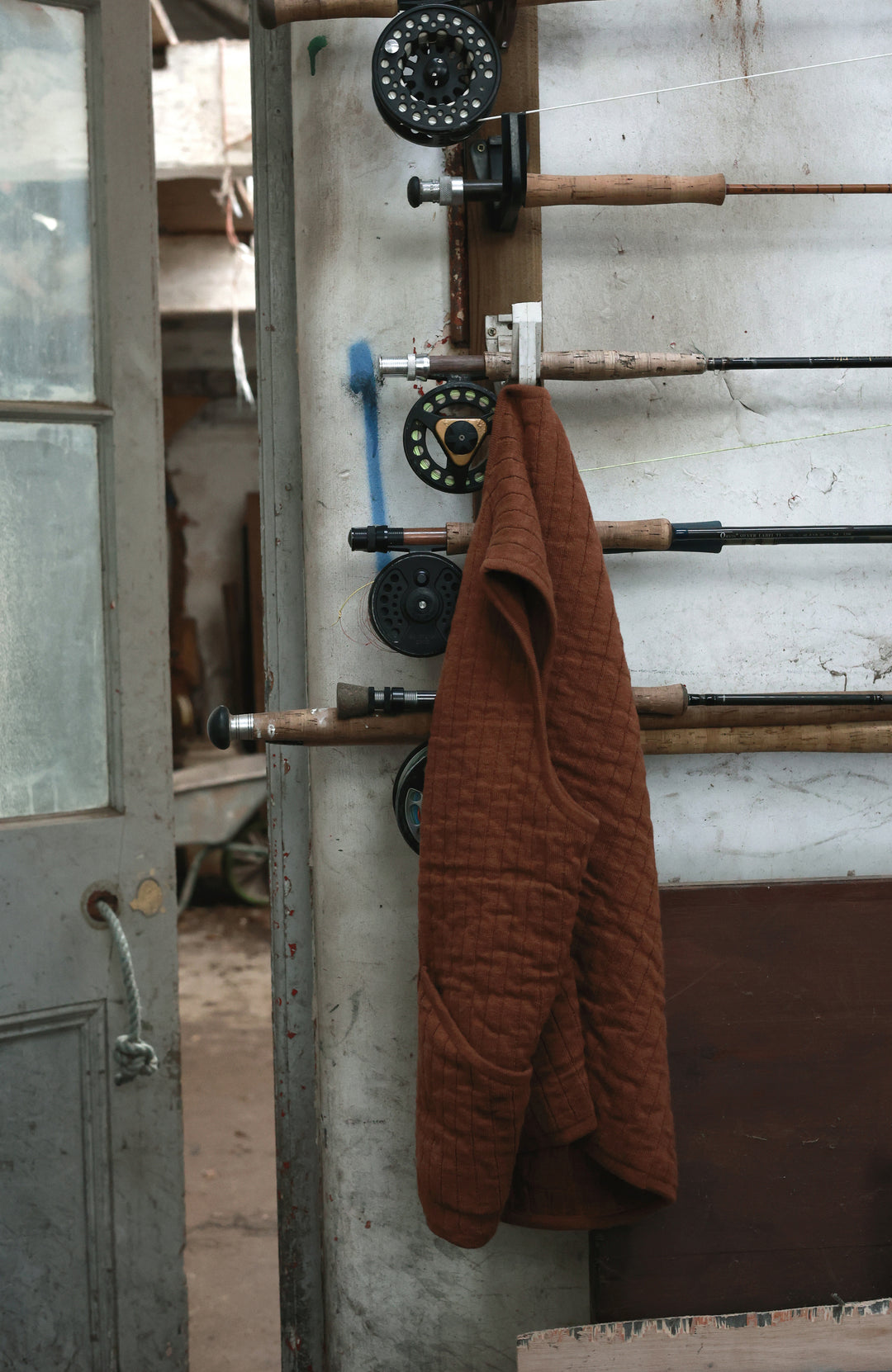 A brown quilted jaket by paul james knitwear hanging from a rustic wall-mounted rod with pulley wheels in an industrial interior setting.