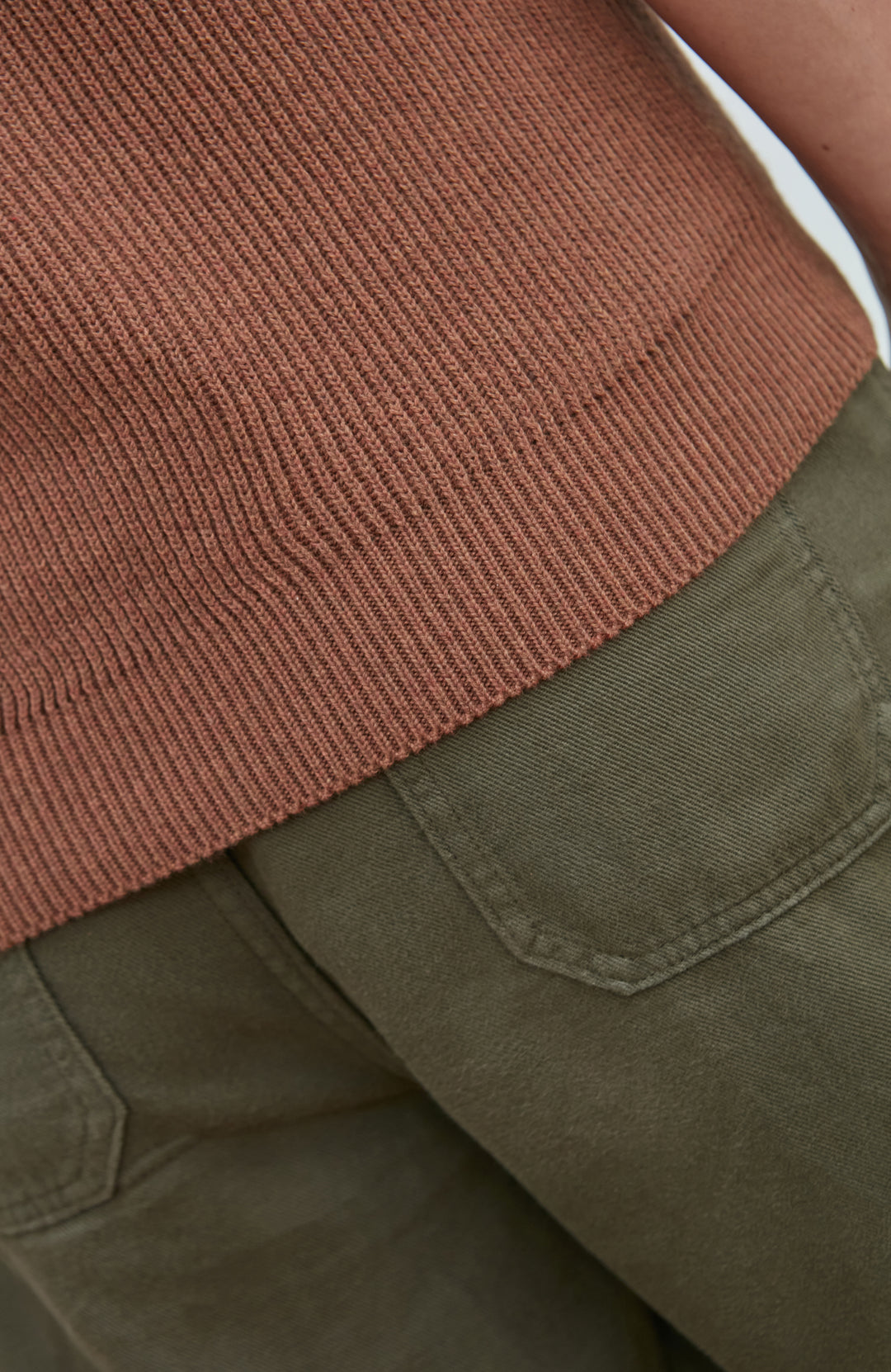 Close-up detail of a ribbed terracotta brown knit top hem paired with olive green pants.