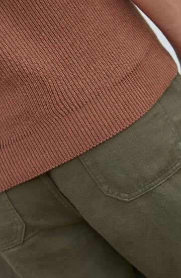 Close-up detail of a ribbed terracotta brown knit top hem paired with olive green pants.